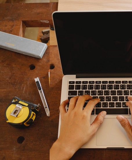Person using a laptop on a workshop bench beside measuring tools